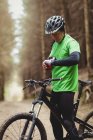 Seitenansicht des Mountainbikers, der die Zeit während der Fahrt im Wald kontrolliert — Stockfoto