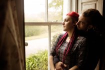 Romântico jovem casal abraçando enquanto olha através da janela em casa — Fotografia de Stock