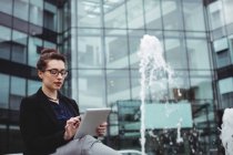 Бізнес-леді, використовуючи цифровий планшет біля фонтану поза офісною будівлею — стокове фото
