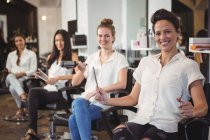 Portrait of smiling multicultural hairdressers sitting on chairs in salon — Stock Photo