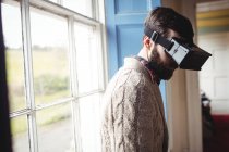 Jovem usando óculos virtuais em casa perto da janela — Fotografia de Stock