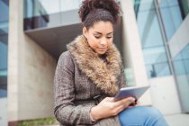 Молодая женщина держит цифровой планшет, сидя напротив здания — стоковое фото