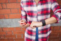 Midsection of woman checking time while holding phone against brick wall — Stock Photo