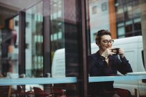 Усміхнена жінка тримає чашку в кафе, яку видно через скло — стокове фото