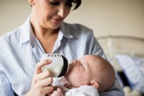 Close up de mãe alimentando bebê com mamadeira de leite em casa — Fotografia de Stock