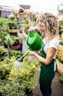 Female florist watering plants with watering can in garden centre — Stock Photo