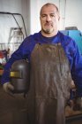 Portrait of welder holding welding helmet in workshop — Stock Photo