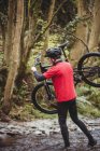 Tutta la lunghezza del motociclista che trasporta la bicicletta mentre attraversa il torrente nella foresta — Foto stock