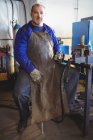 Retrato de soldador sosteniendo sierra eléctrica en taller - foto de stock