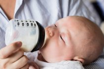Abgeschnittenes Bild von Mutter, die Baby zu Hause mit Milchflasche füttert — Stockfoto