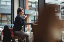 Junge Frau trinkt Kaffee, während sie auf Stuhl im Café sitzt — Stockfoto
