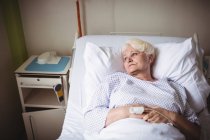 Задумчивая пожилая женщина на кровати в больнице — стоковое фото