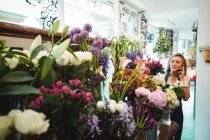 Жіночий флорист розмовляє на мобільному телефоні при розташуванні квітів у квітковому магазині — стокове фото