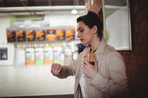 Giovane donna che controlla l'ora mentre tiene il drink alla stazione ferroviaria — Foto stock