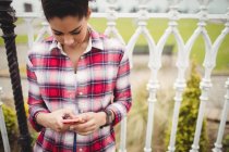 Hübsche junge Frau benutzt Smartphone, während sie sich an Geländer lehnt — Stockfoto