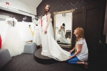 Woman trying on wedding dress in studio with assistance of creative designer — Stock Photo