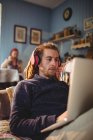Hipster homem usando laptop enquanto ouve música em casa — Fotografia de Stock