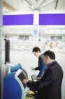 Ділові люди, які використовують самообслуговування реєстраційних машин в аеропорту — стокове фото