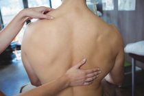 Imagen recortada de fisioterapeuta femenina dando masaje de espalda a un paciente masculino en la clínica - foto de stock