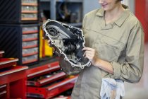 Imagen recortada de mecánico femenino sosteniendo piezas de repuesto en el garaje de reparación - foto de stock