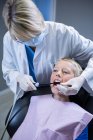 Dentista examinando a un paciente joven con herramientas en la clínica dental - foto de stock
