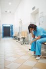 Грустная медсестра, сидящая на деревянном стуле в коридоре больницы — стоковое фото