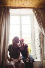 Young hipster couple sitting against window at home — Stock Photo