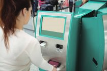 Viajero que utiliza la máquina de facturación de autoservicio en el aeropuerto - foto de stock