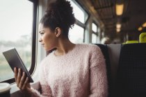 Жінка дивиться крізь вікно, тримаючи цифровий планшет у потязі — стокове фото