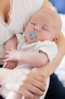 Cropped image of baby with dummy sleeping in mother arms at home — Stock Photo