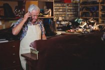 Senior shoemaker talking on the mobile phone in workshop — Stock Photo