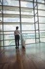Rear view of businesswoman with luggage looking through glass window at airport — Stock Photo