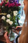 Imagen recortada de la floristería femenina recortando hojas de flores en su floristería - foto de stock