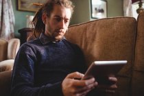 Giovane uomo che utilizza tablet digitale mentre seduto sul divano a casa — Foto stock