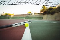 Tennis racket and ball on center line in green and brown court — Stock Photo