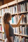 Frau entfernt Buch aus Bücherregal in Bibliothek — Stockfoto