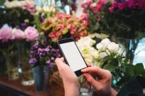 Mani di fiorista femminile che tiene il telefono cellulare nel negozio di fiori — Foto stock