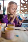 Внимательная девушка рисует на чаше в мастерской по керамике — стоковое фото