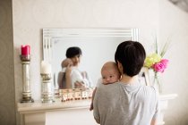 Madre che porta il suo bambino e in piedi davanti allo specchio a casa — Foto stock