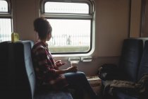 Жінка дивиться крізь вікно, тримаючи мобільний телефон у потязі — стокове фото