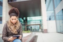 Молода жінка використовує цифровий планшет, сидячи проти будівництва — стокове фото