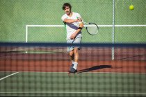 Mann spielt Tennis auf Sportplatz im Sonnenlicht — Stockfoto