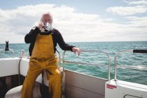 Рыбак пьет кофе из чашки на лодке — стоковое фото
