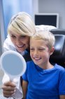 Dentista sorridente e giovane paziente che si guarda allo specchio alla clinica dentistica — Foto stock