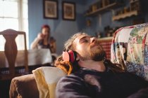 Uomo hipster che ascolta musica mentre si rilassa sul divano di casa — Foto stock