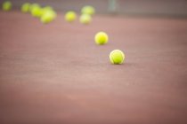 Теннисные мячи лежат на коричневом спортивном корте — стоковое фото
