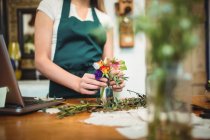 Partie médiane de fleuriste femelle arrangeant des fleurs dans une bouteille à sa boutique de fleurs — Photo de stock