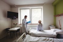 Doutor interagindo sobre um relatório com a mulher idosa no hospital — Fotografia de Stock