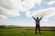 Full length of man standing with arms raised against cloudy sky — Stock Photo