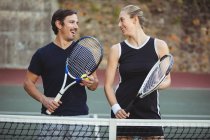 Jugadores de tenis felices de pie en la cancha con raquetas - foto de stock